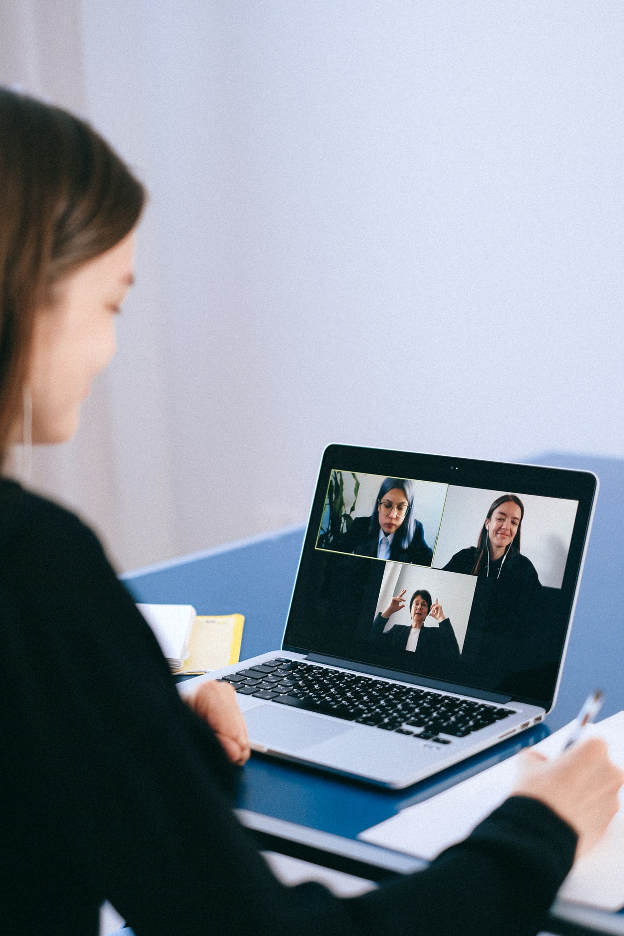 Woman seen in an over the shoulder shot during a virtual meeting on her laptop with three others pictured on screen